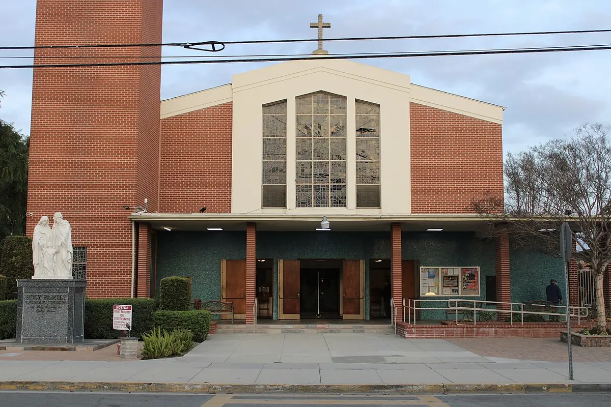 Fachada de ladrillo de la iglesia Holy Family de Artesia, con su gran ventanal central y el campanario a la izquierda