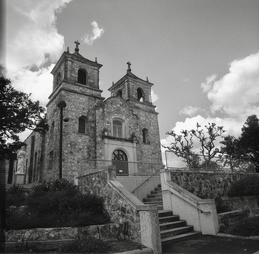 Iglesia de San Pedro Apóstol de Boerne, de piedra, con dos campanarios y escalinata, en blanco y negro